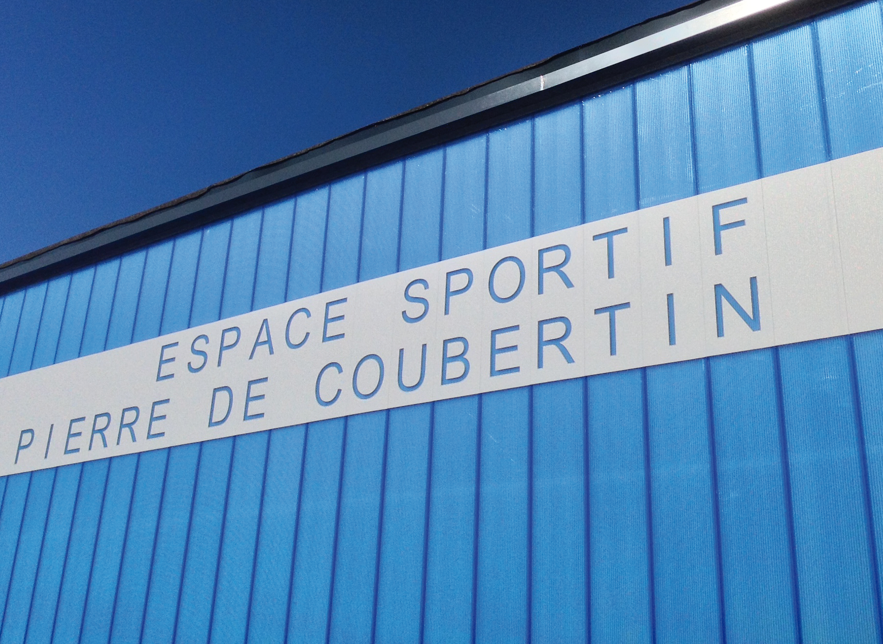 Centre sportif Pierre de Coubertin dont la façade est composée de plaques de polycarbonate emboîtable bleues